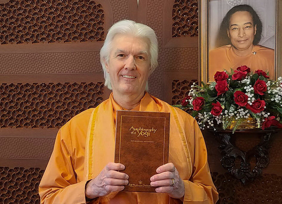 Brother Chidananda holding Autobiography of a Yogi Deluxe Edition